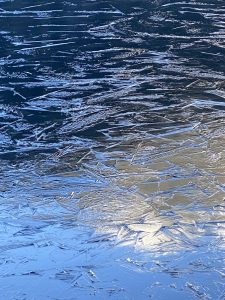 eine gefrorene Wasser-Oberfläche in dem sich im unteren rechten Bereich die Sonne und ein bisschen Umgebung spiegelt, die aber nicht genau erkennbar ist